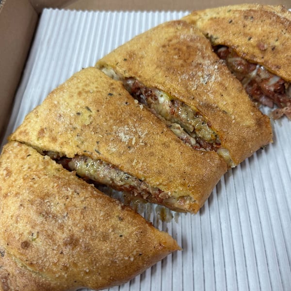Four slices of Hindsight Pizza's golden-brown calzone, filled with melted cheese and meat, in a takeout box.