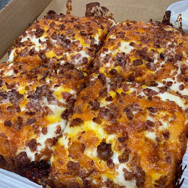 Four square slices of Hindsight Pizza, topped with melted cheese and crispy bacon bits, in a cardboard box.