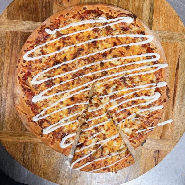 Hindsight Pizza's BBQ chicken pizza with ranch drizzle, a slice removed, on a wooden board.