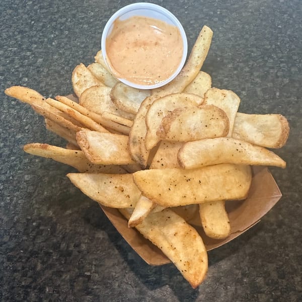 A paper tray filled with seasoned potato wedges and a small cup of dipping sauce.