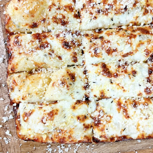 Close-up of Hindsight Pizza's cheesy garlic breadsticks, topped with parmesan and herbs.