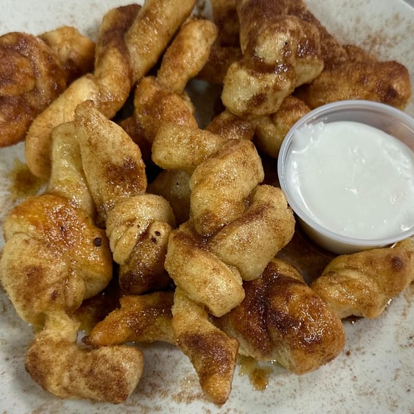 Hindsight Pizza's cinnamon twists, glistening with glaze and cinnamon sugar, served with a side of white icing.
