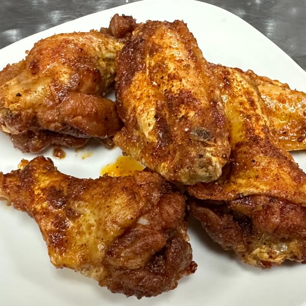 Close-up of crispy, seasoned chicken wings on a white plate, glistening with sauce.