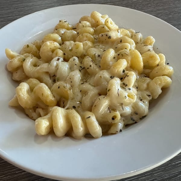 Creamy macaroni and cheese with herbs in a white bowl on a wooden table.
